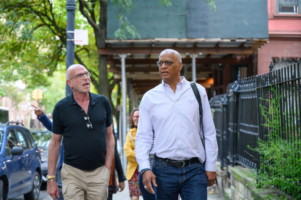 Two men walking and talking on the sidewalk with scaffolding in the background.