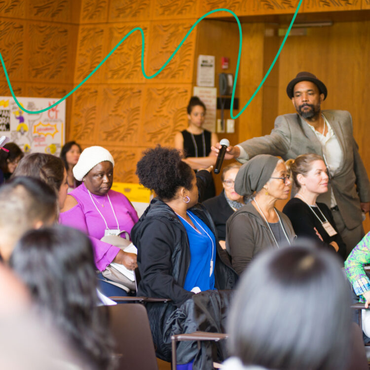 A group of people attend a forum. A man hands a microphone to an audience member.